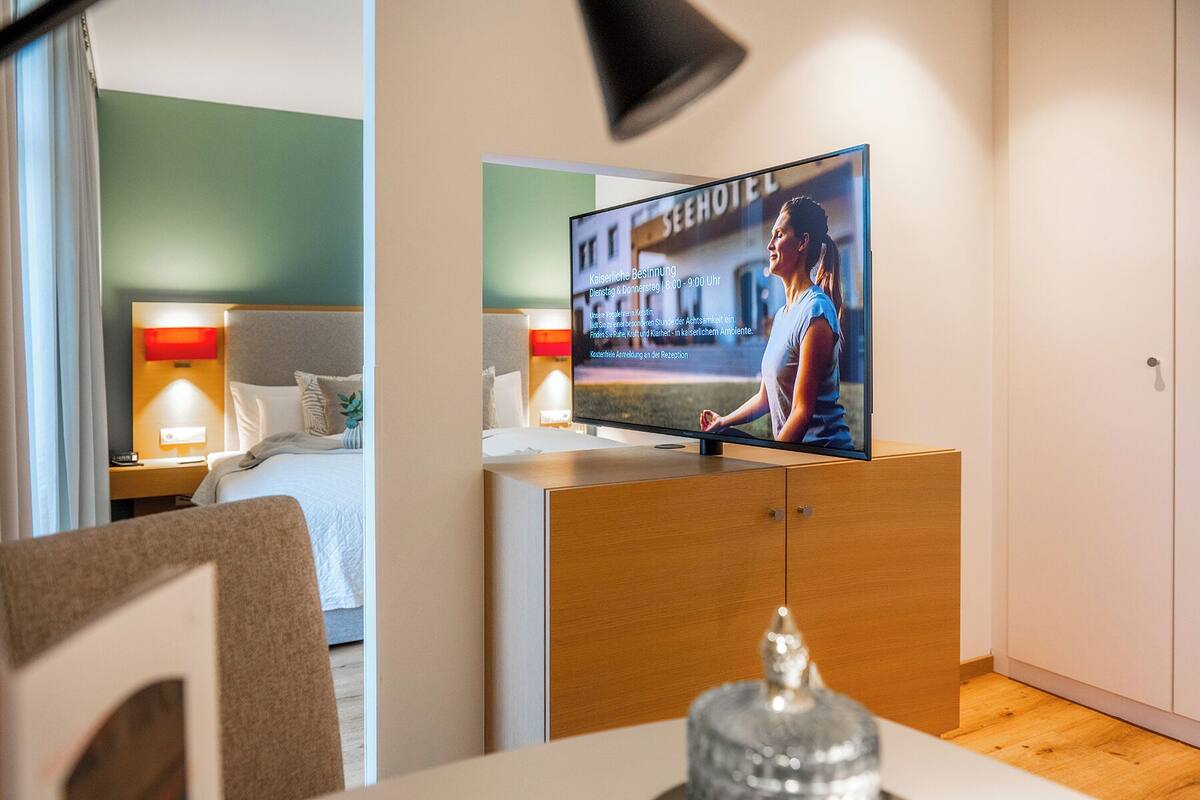 A hotel room with a bed, a TV on a wooden cabinet, and a nightstand with a lamp.