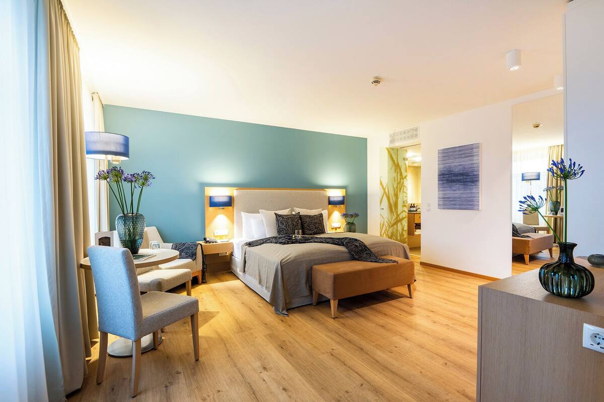 A modern hotel room with a large bed, bedside tables, a chair, and a desk.