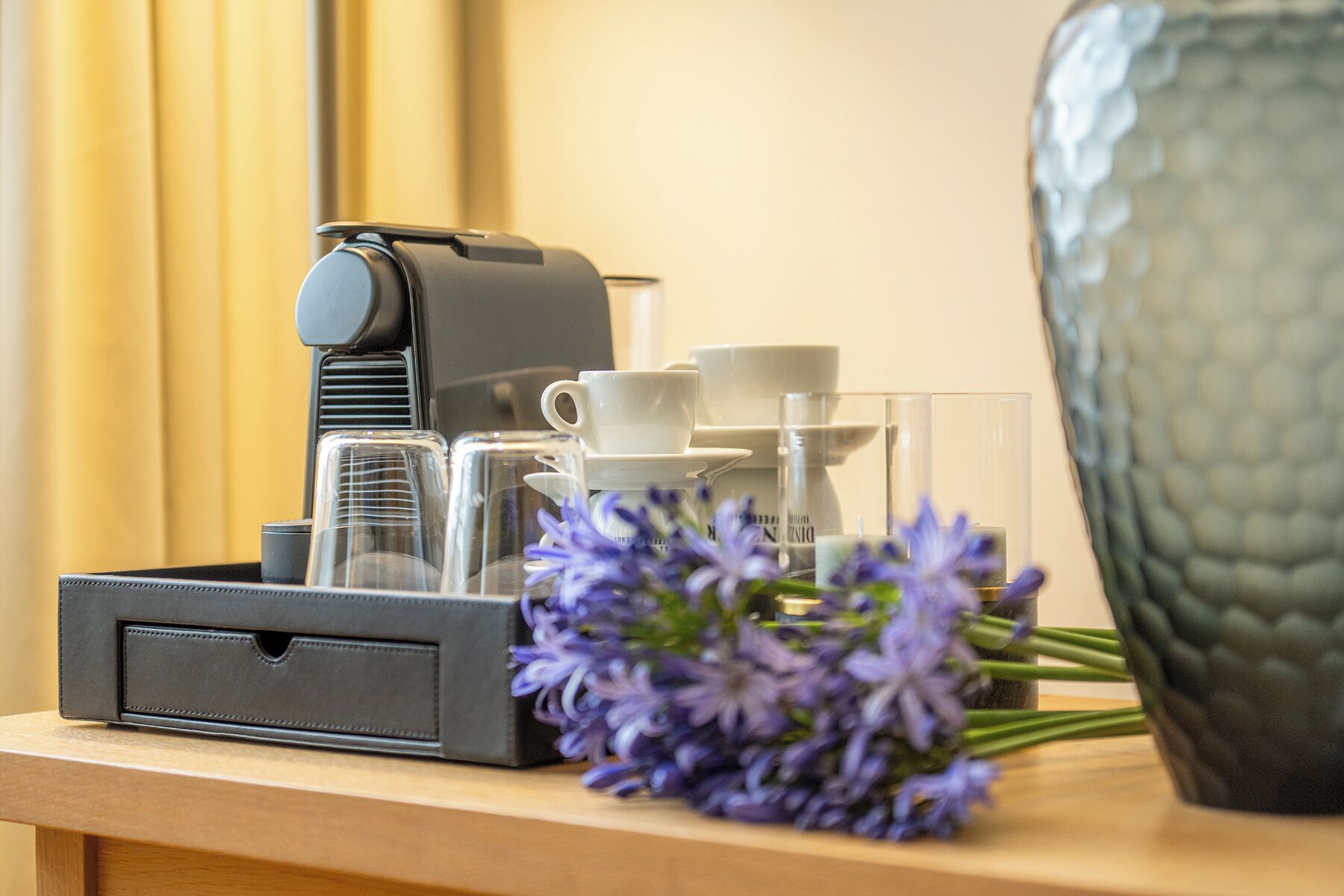 Máquina de café, chávenas, copos e um vaso com flores sobre uma superfície de madeira.