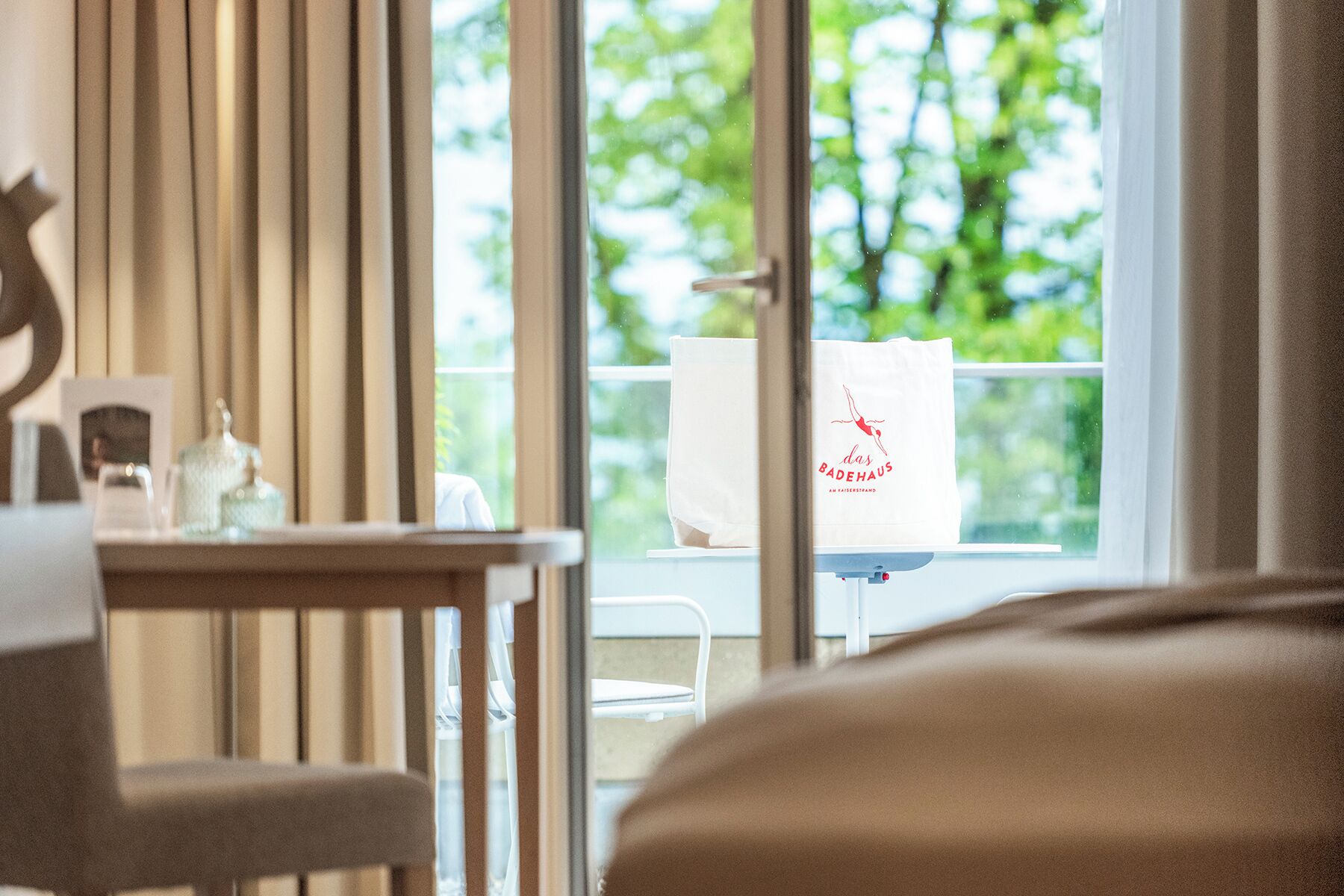 Ein Hotelzimmer mit Esstisch, einem Stuhl, einem Fenster mit Blick auf Grünflächen und einer weißen Tasche mit Aufdruck.