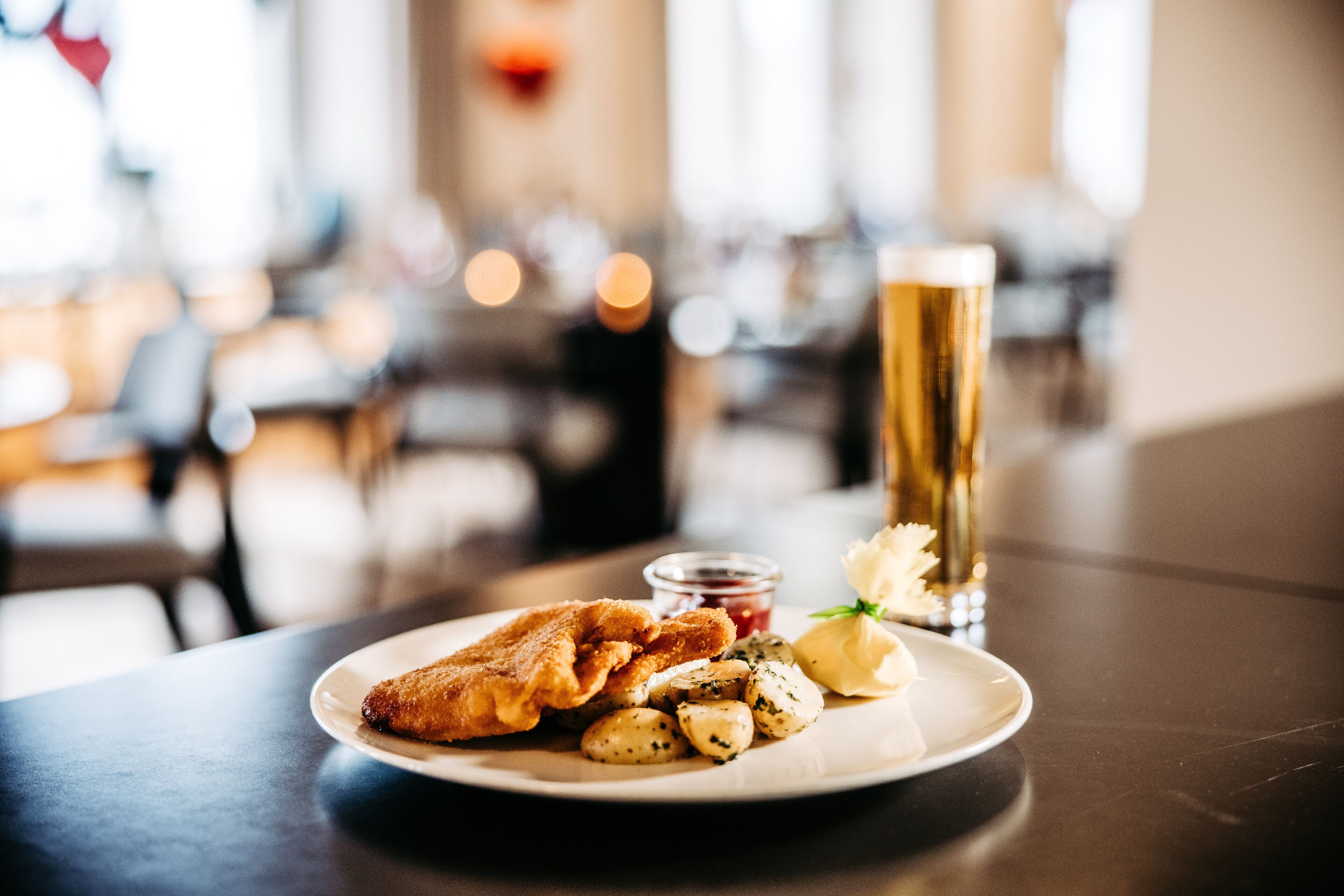 A plate with fried food, boiled potatoes, and a glass of beer on a table in a restaurant.
