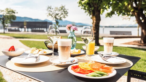 Una mesa exterior con platos de comida, vasos de bebidas y un florero con flores.