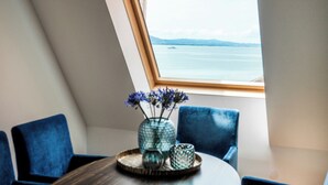 Un área de comedor con una mesa, sillas, un florero con flores y vista a una masa de agua a través de una ventana.