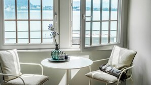 Una habitación con vistas a un lago, una pequeña mesa redonda con un florero y adornos, y dos sillones tapizados.