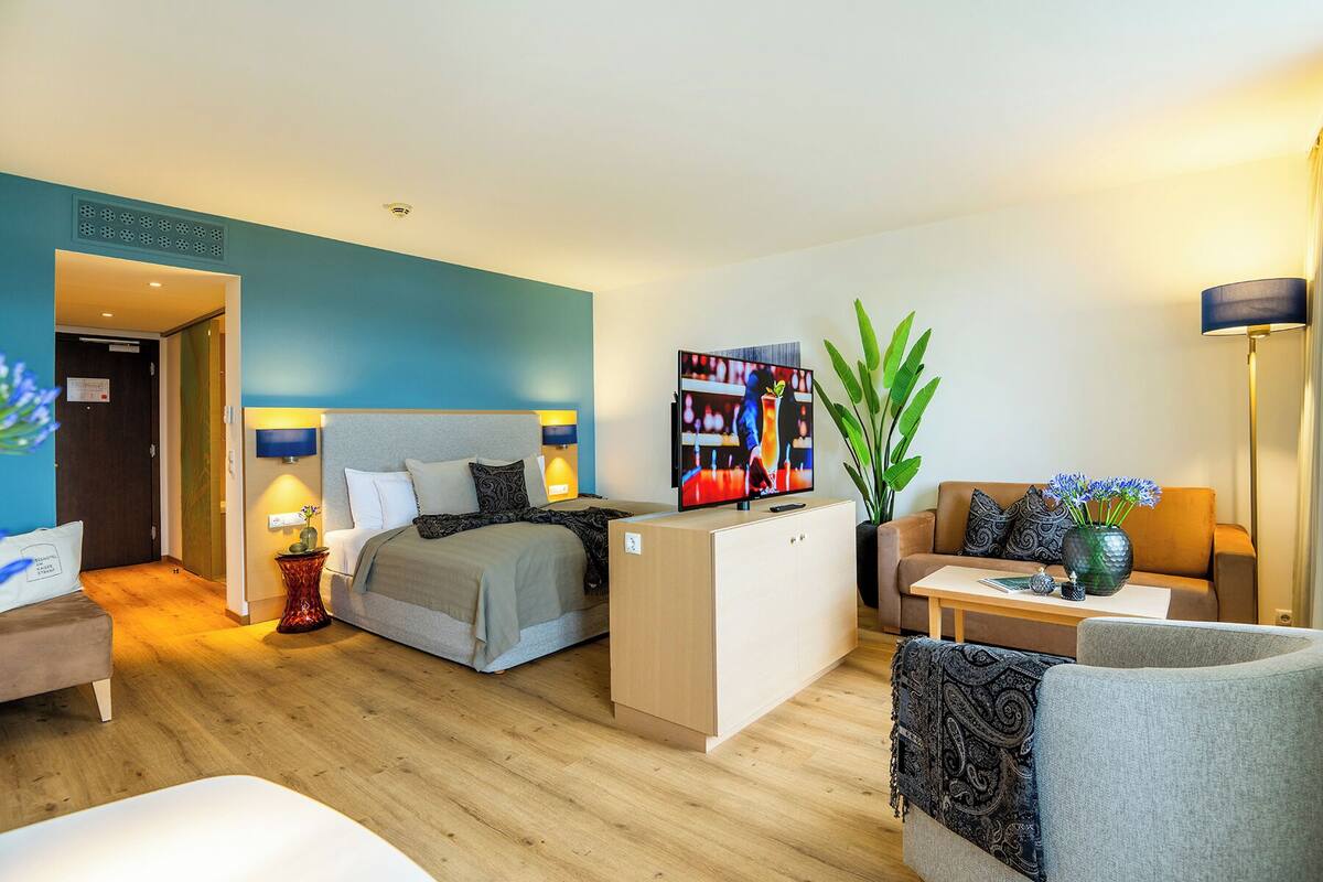 A modern hotel room with a bed, a desk, a sofa, and a TV.