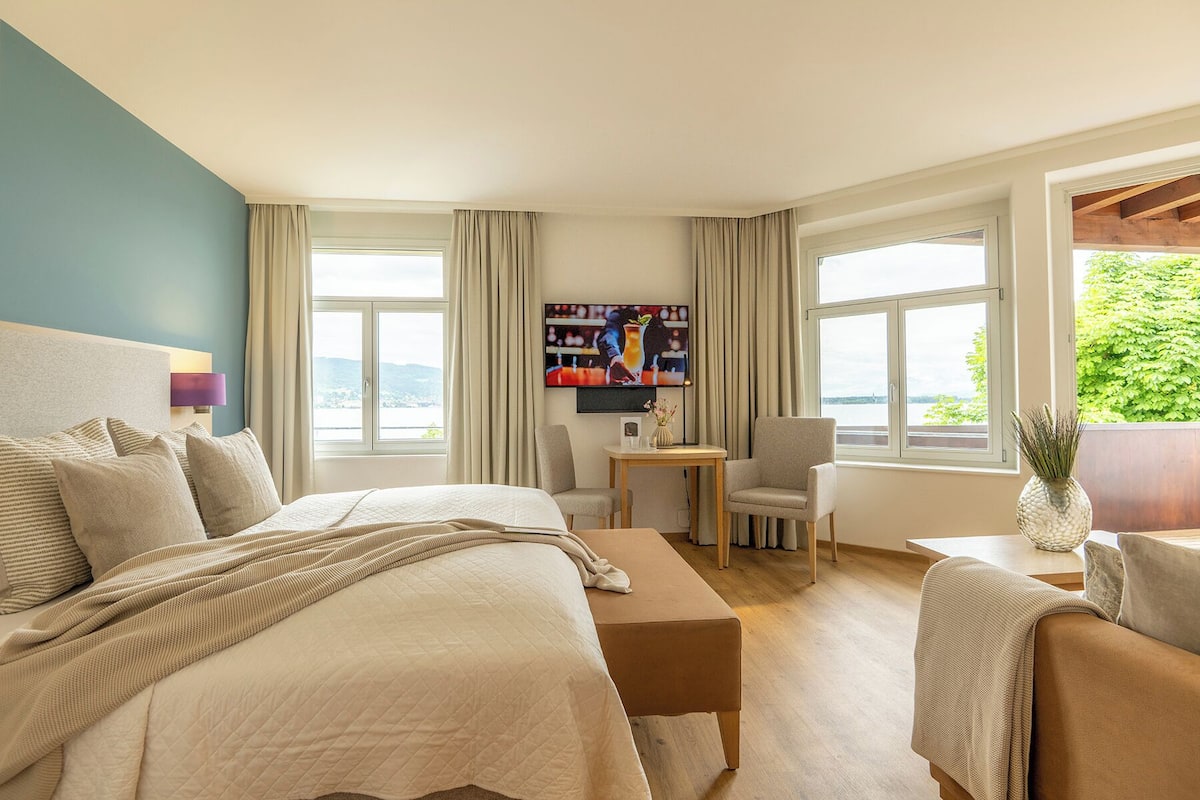 A hotel room with a large bed, a desk, two chairs, and a TV on the wall.