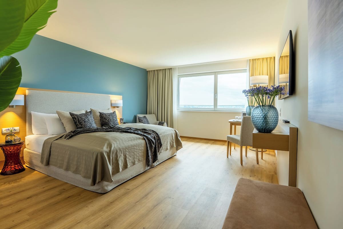 A modern hotel room with a large bed, a desk, and a window with curtains.