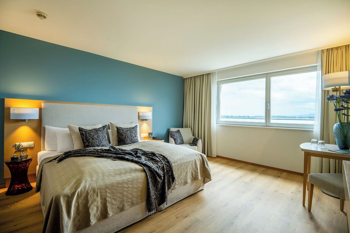 A modern hotel room with a large bed, a desk, and a view of the city.