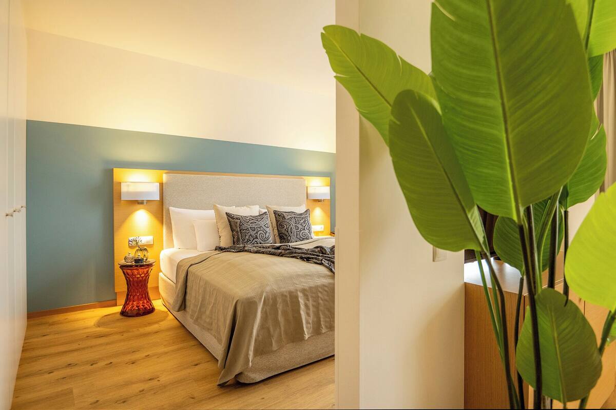 A bedroom with a bed, bedside lamps, and a large green plant.