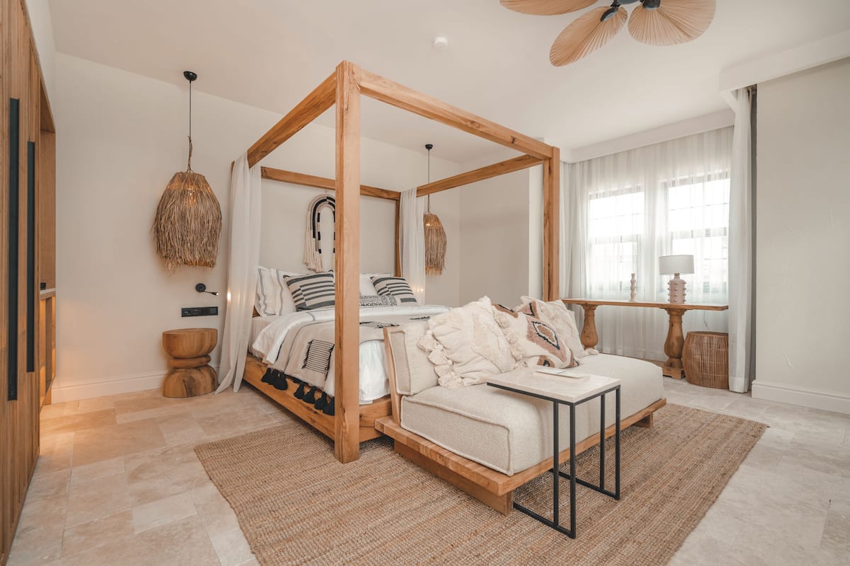 A bedroom with a four-poster bed, a sofa, a small table, and a bedside table with a lamp.