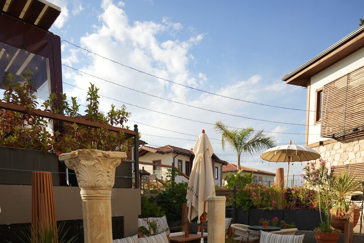 An outdoor patio area with wooden furniture, a glass table, and potted plants.
