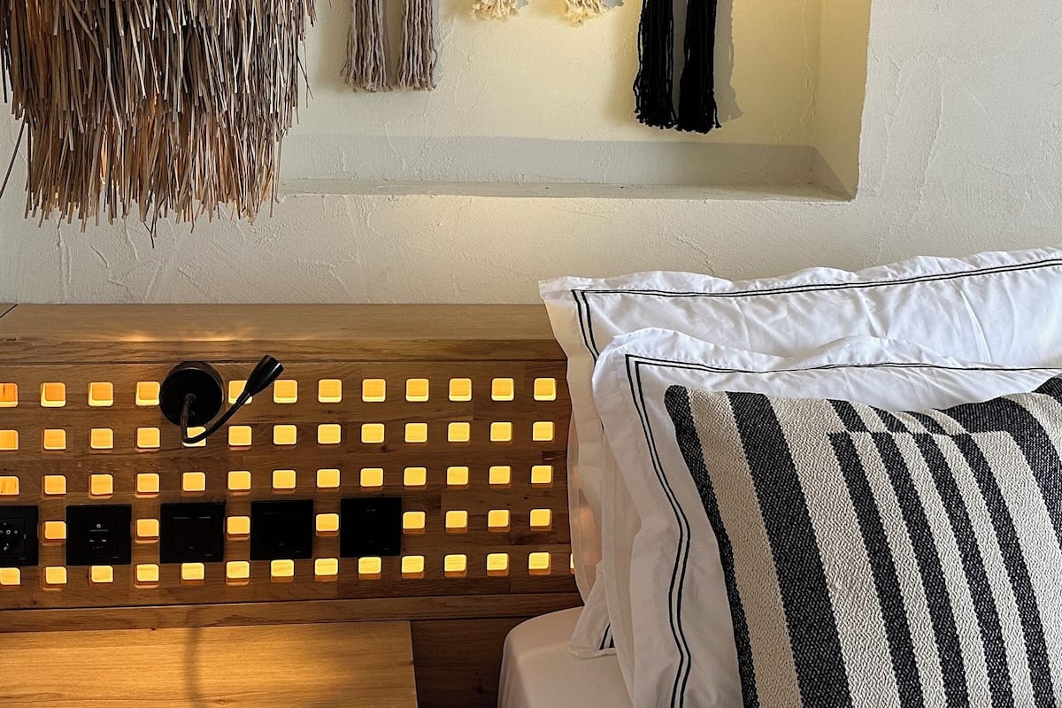 A bedroom with a wooden bench, a hanging light fixture, and wall-mounted decorative items.
