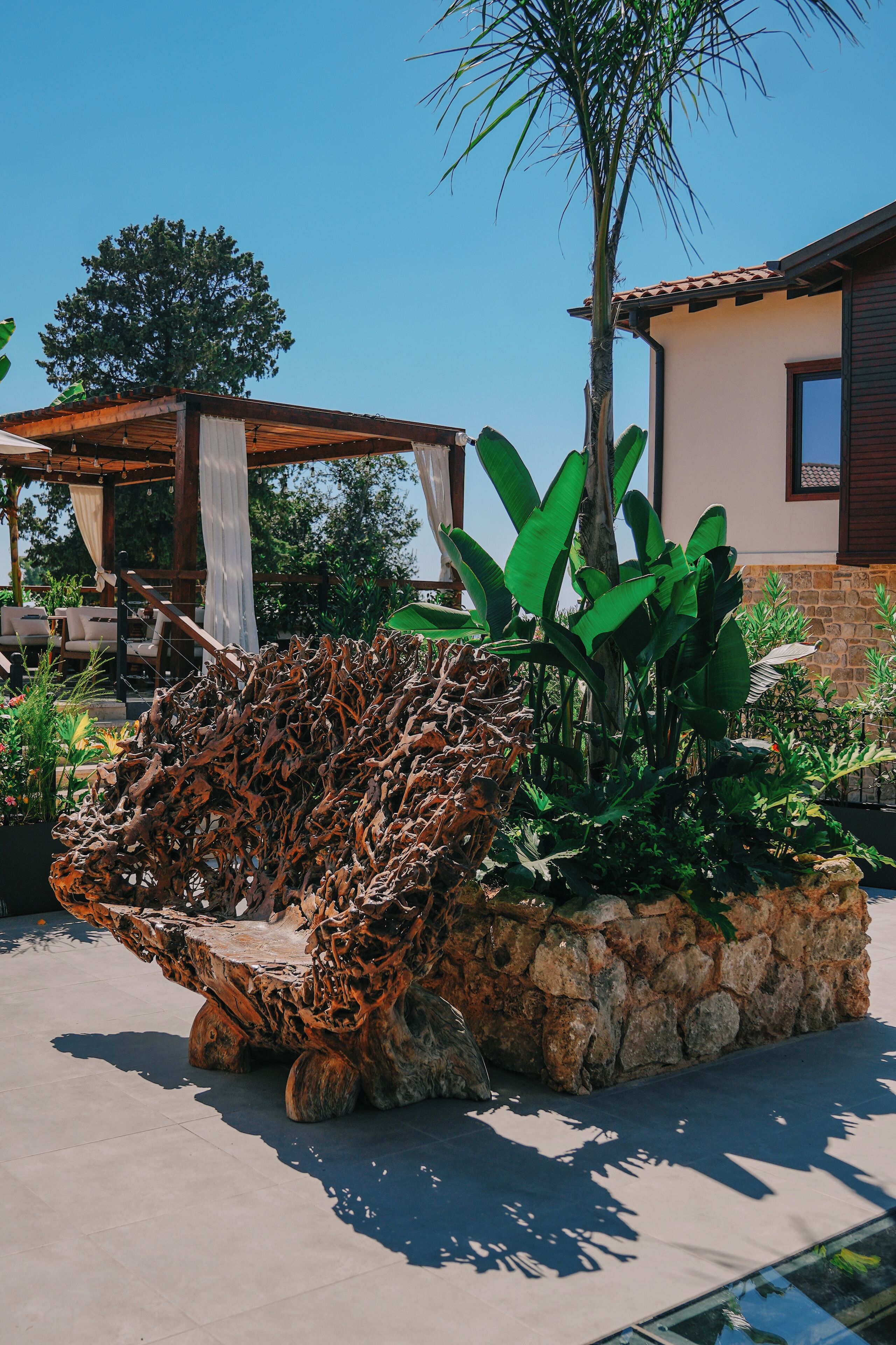 Un espacio al aire libre rústico con una silla de madera original, rodeado de exuberante follaje y una jardinera de piedra.