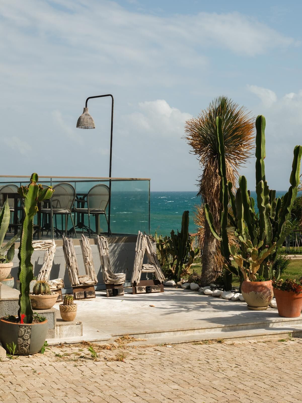 Un patio con cactus en macetas, una farola y vista al océano.