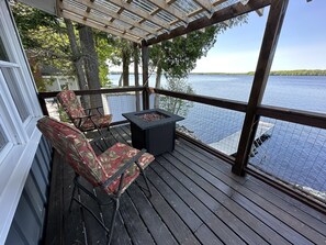 A wooden deck with a pergola, two floral chairs, and a fire pit.