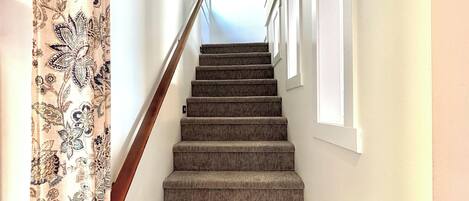 Una escalera empapelada con barandilla, que conduce a un rellano con una obra de arte enmarco.