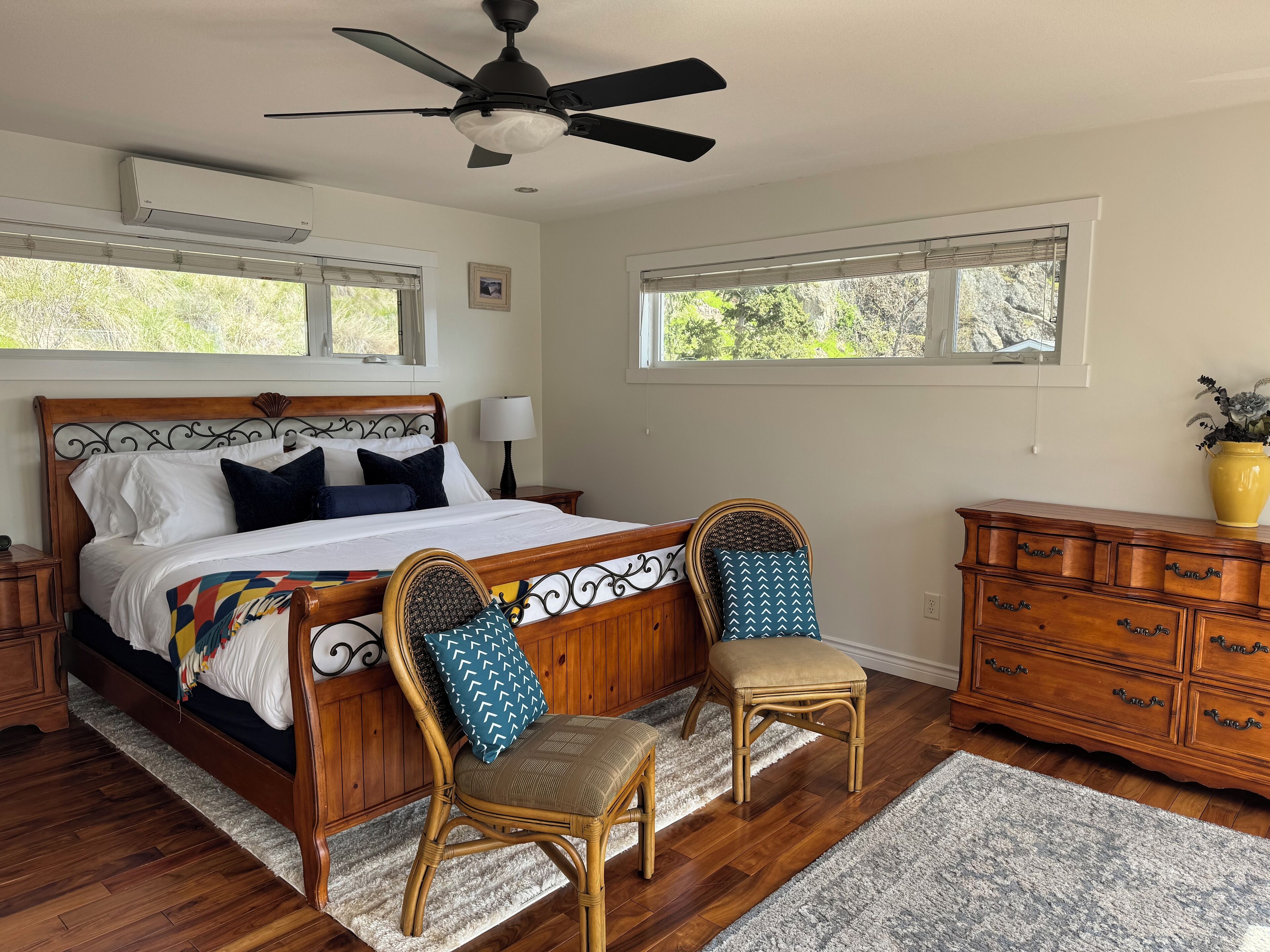 Une chambre à coucher avec un lit en bois, deux chaises, une commode et un ventilateur de plafond.