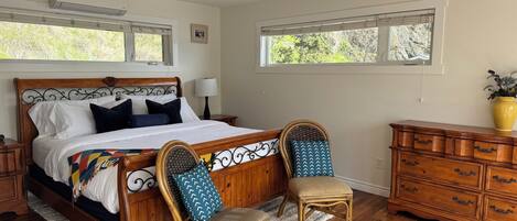 Un dormitorio con cama de madera, dos sillas, un aparador y un ventilador de techo.