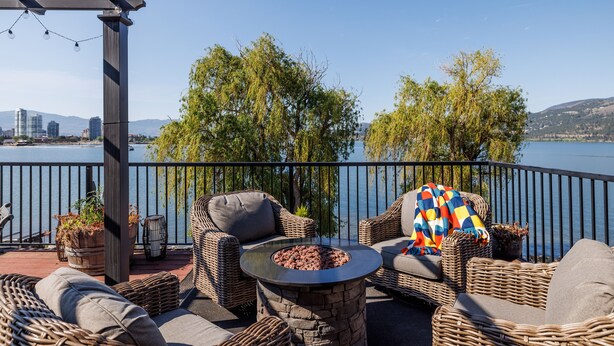 Un balcon agrémenté de meubles en osier, d’un foyer en pierre et offrant une vue sur un lac et le paysage urbain.