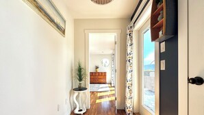 Un couloir avec un plancher en bois, une plante en pot, une petite table et une porte donnant sur un balcon.