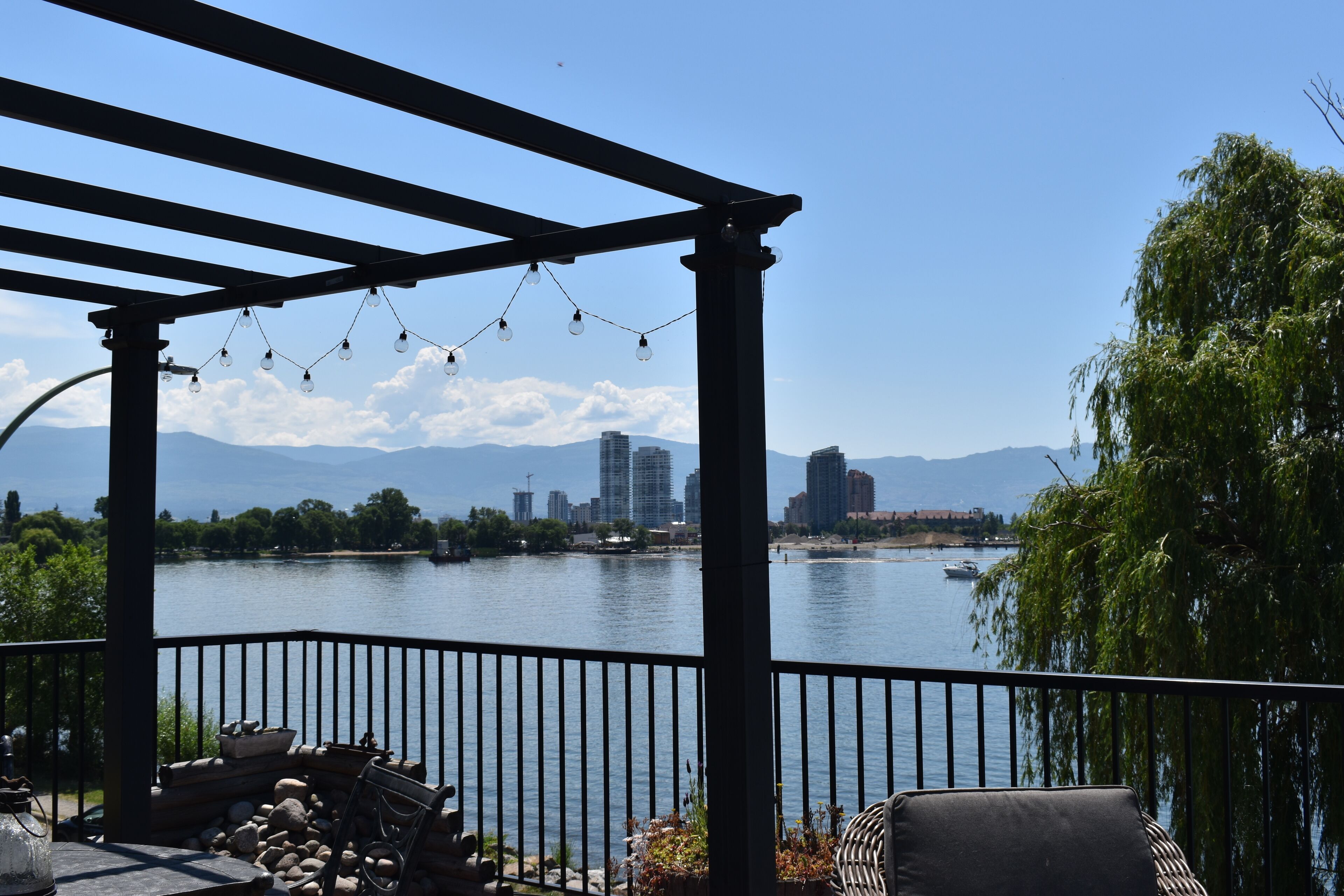 A covered outdoor area with a view of a lake, a city skyline, and mountains in the distance.
