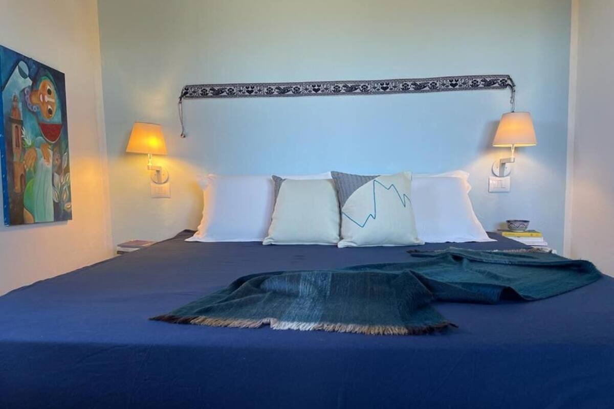 A bed with a blue bedspread, two pillows, a decorative headboard, and two wall-mounted lamps.