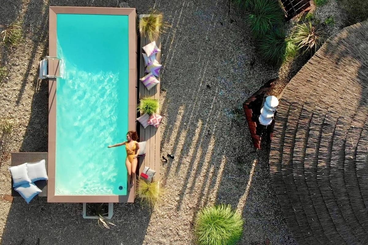 An aerial view of a rectangular pool with clear water, surrounded by a wooden deck and lounge chairs.