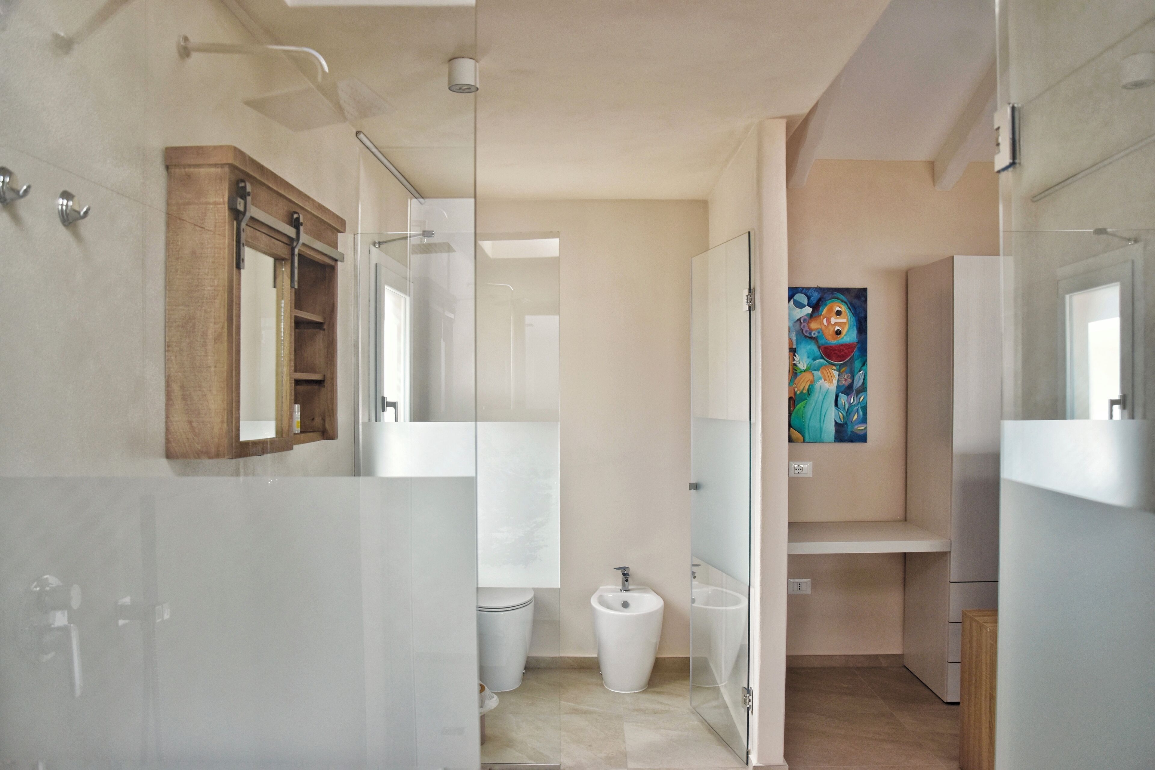 Un baño moderno con cabina de ducha de vidrio, un armario de medicinas de madera, un lavamanos blanco y un cuadro en la pared.