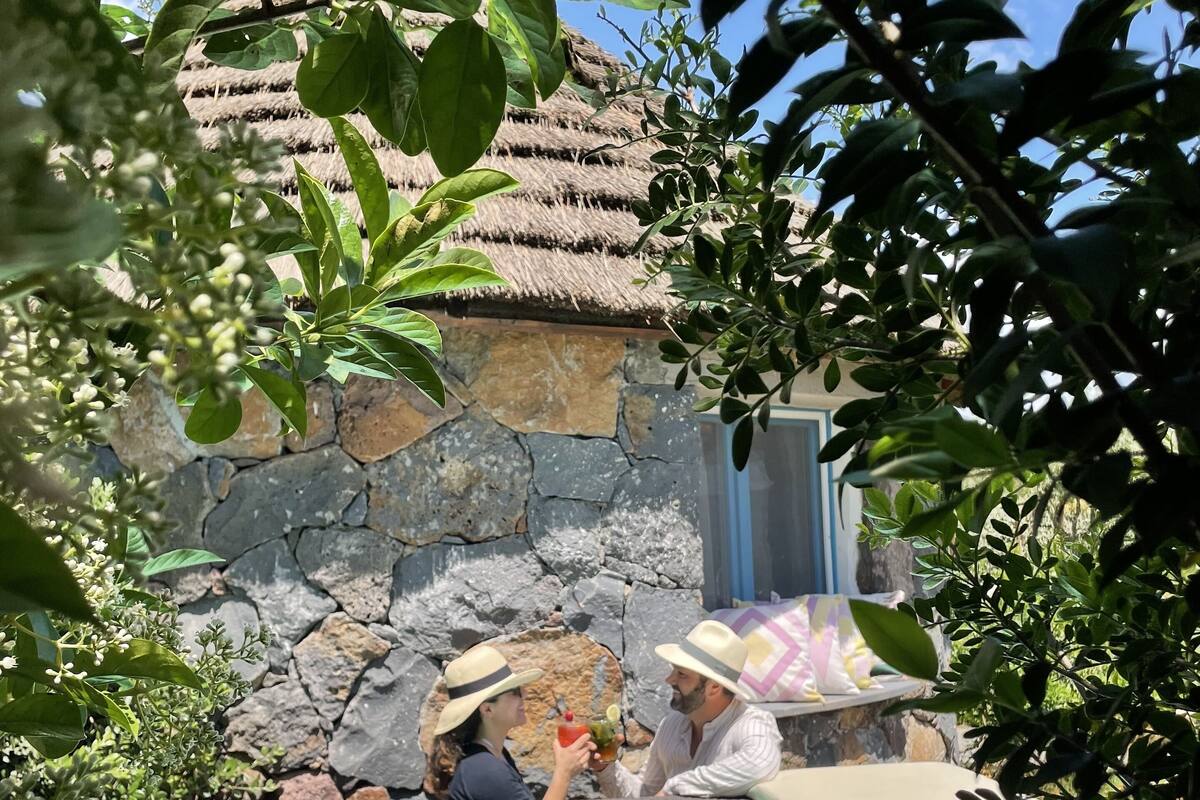 A pool area with a stone wall and a thatched roof structure.