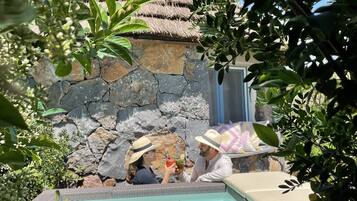 A pool area with a stone wall and a thatched roof structure.