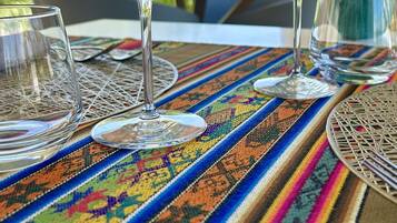 Two empty wine glasses on a colorful woven tablecloth with a view of greenery and a building in the background.