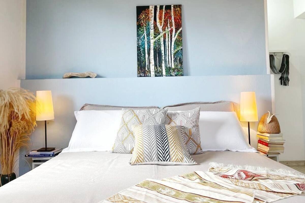 A neatly made bed with patterned pillows, a wall-mounted painting, and a bedside lamp.