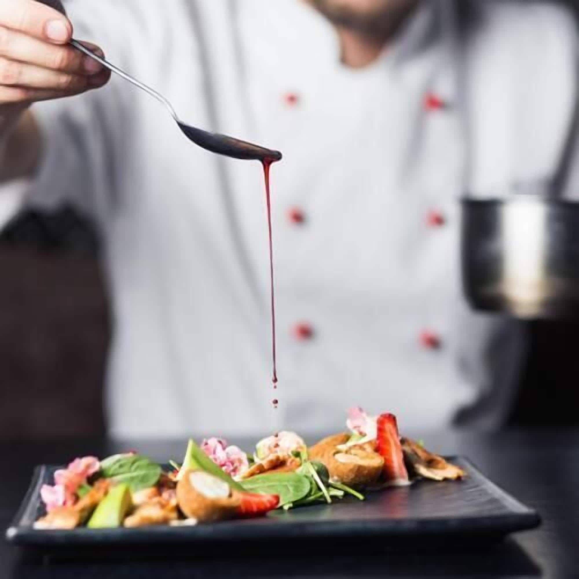 Un chef sirviendo salsa sobre un plato.