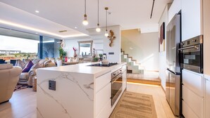 Una cocina moderna con una isla de mármol, horno empotrado y electrodomésticos de acero inoxidable. Cuenta con una zona de estar con sofá y una mesa de centro.