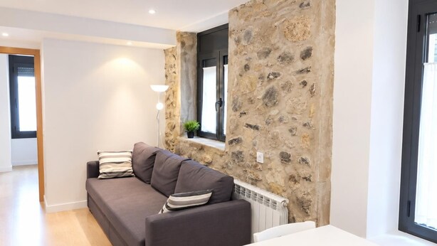Ein modernes Wohnzimmer mit einer Wand aus Stein, einem grauen Sofa, einem weißen Tisch und einem Fenster mit Blick.