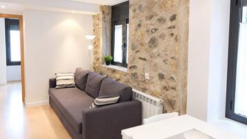 Una sala de estar moderna con una pared de acento de piedra, un sofá gris, una mesa blanca y un ventanal con vistas.