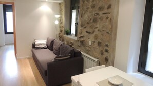 Un salon moderne avec un mur d’accent en pierre, un canapé foncé, une table blanche et une fenêtre avec des stores.
