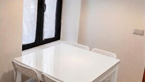 Ein weißer Tisch mit vier Stühlen, ein Fenster mit schwarzem Rahmen und ein Lichtschalter an der Wand.