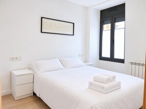A minimalist bedroom with a bed, bedside table, and a framed picture on the wall. - Apartment 2 rooms in Puigcerdà Center (Accessible) (Puigcerdà)