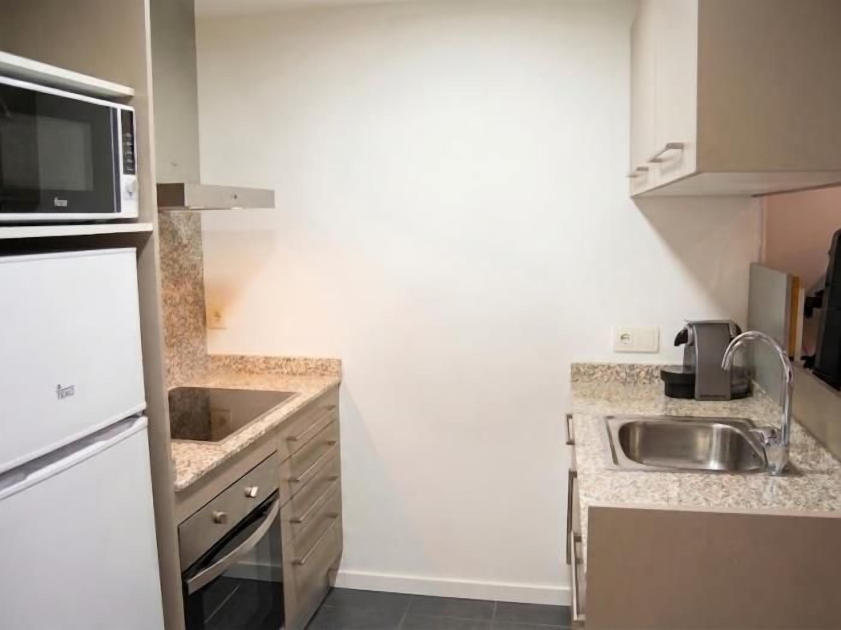 Una cocina compacta con microondas, horno, pileta y encimera de granito.