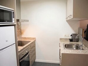 A compact kitchen with a microwave, oven, sink, and granite countertop.