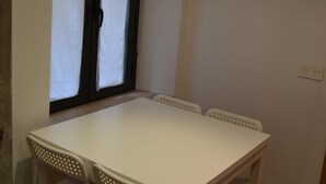 Une pièce avec une table blanche et quatre chaises, une fenêtre avec des rideaux et un interrupteur sur le mur.