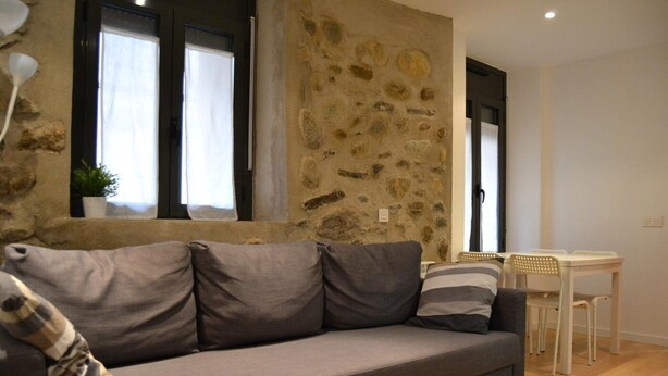 Un salon moderne avec un mur en pierre, un canapé gris et une petite table à manger avec des chaises.