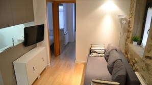Un salon moderne avec un canapé gris, un téléviseur à écran plat fixé sur un meuble blanc et un mur d’accent en pierre.