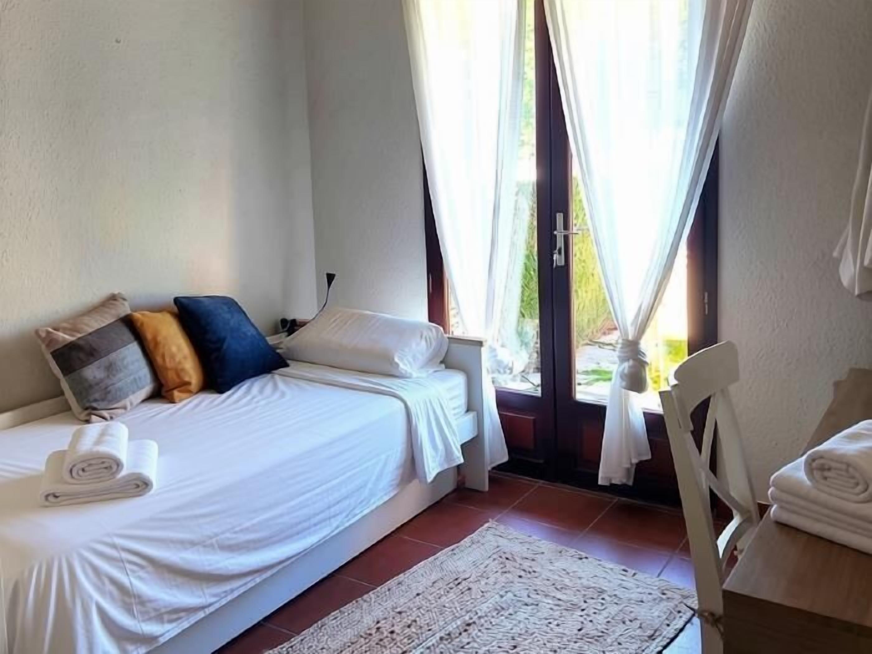 Une chambre à coucher avec un lit, une chaise, une fenêtre avec des rideaux et une vue sur l’extérieur.