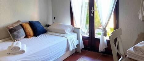 Une chambre à coucher avec un lit, une chaise, une fenêtre avec des rideaux et une vue sur l’extérieur.