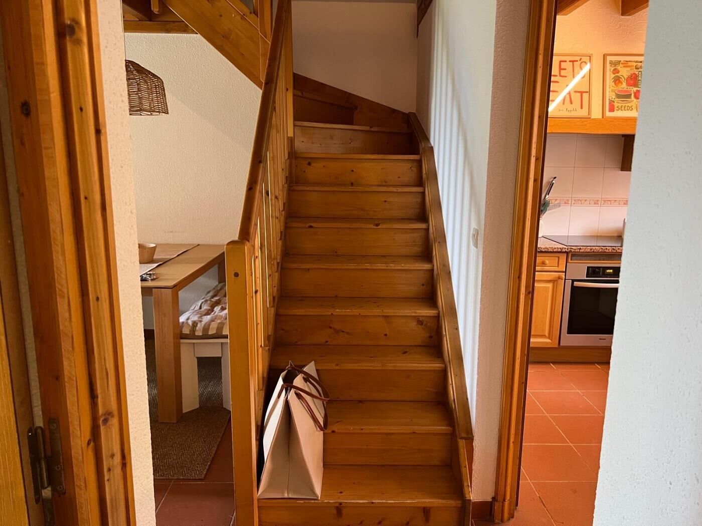 Eine Holztret Treppe führt zu einem Küchenbereich mit Holzschränken und Fliesenboden.