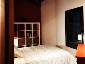 A bedroom with a bed, a white headboard, a window, and a bookshelf.