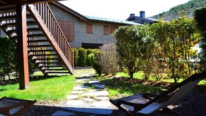 A stone pathway leading to a wooden staircase, surrounded by lush greenery and a building with a stone facade. - Ground Floor 3 rooms Pool, Fireplace, Garden & Wi-Fi (Queixans)