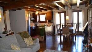 A cozy living room with a grey sofa, a dining table with chairs, a kitchen area with a microwave, and a staircase leading to another level. - Ground Floor 3 rooms Pool, Fireplace, Garden & Wi-Fi (Queixans)